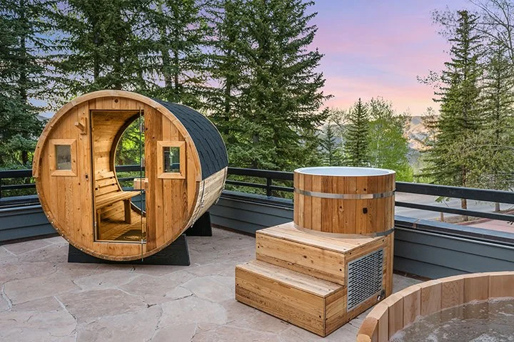 Wooden outdoor hot tub and sauna on a balcony with forest view at sunset
