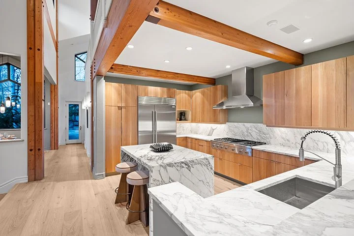 Modern kitchen with wooden cabinets, marble countertops, a large center island, stainless steel appliances, and exposed wooden beams on the ceiling.