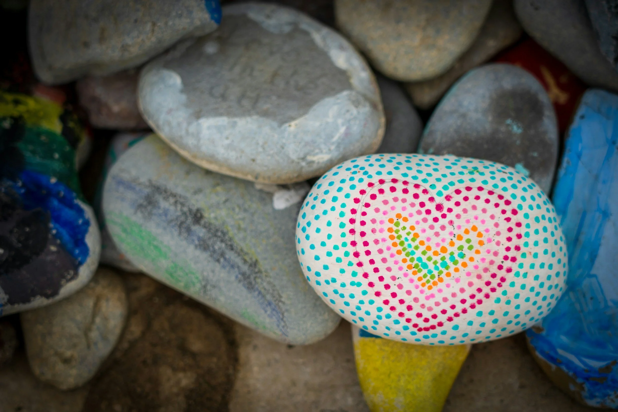 Colorful painted rocks, including one with multicolored polka dots arranged in a flower pattern.