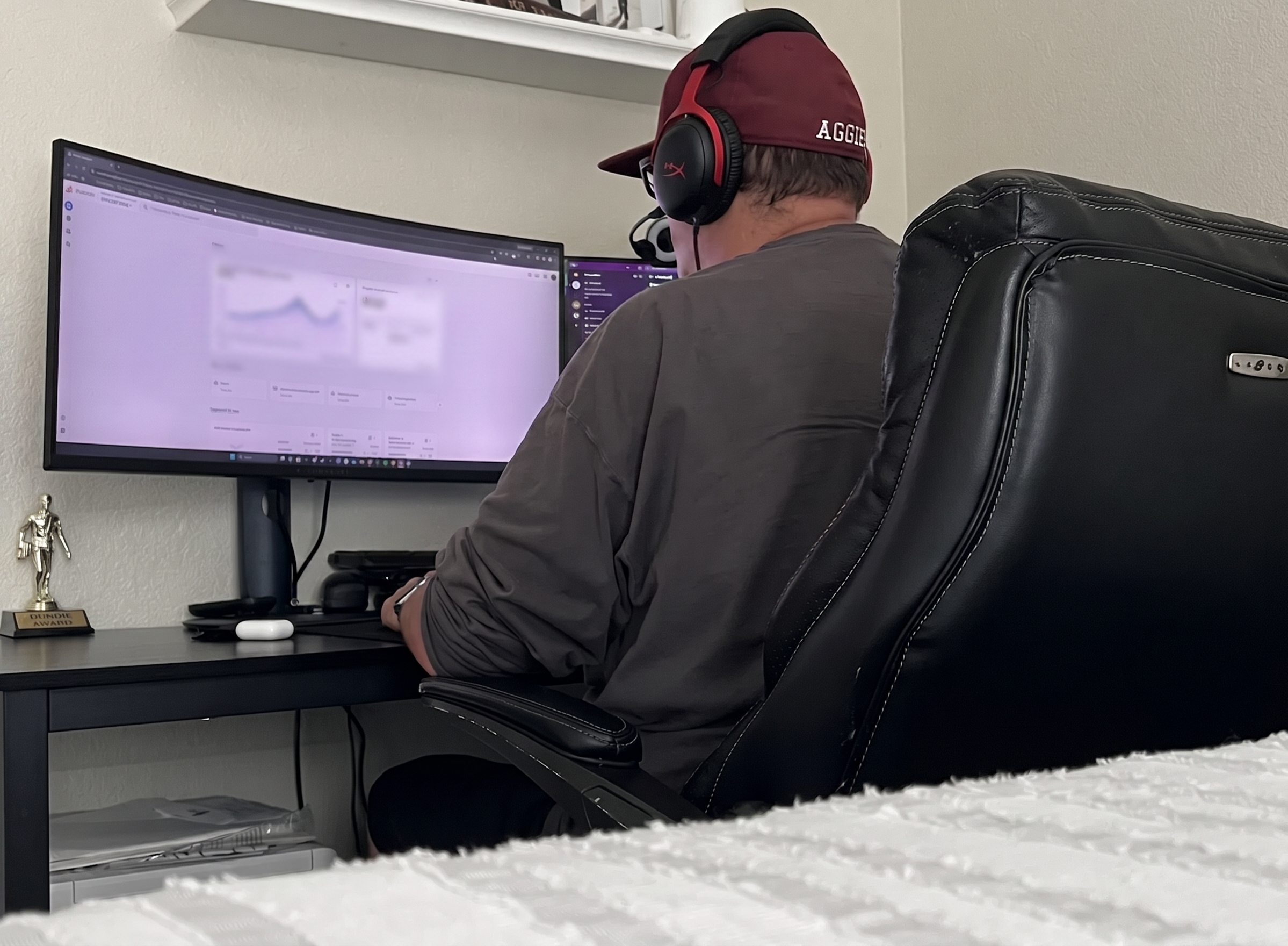 Person wearing headphones working on a computer at a desk with dual monitors, analyzing data for digital marketing strategies, showcasing a home office setup.