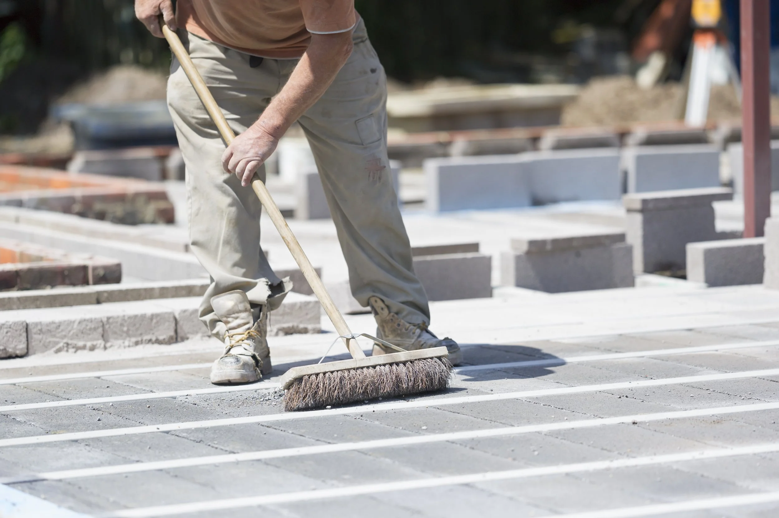 A construction worker sweeping freshly laid concrete on a sidewalk with a broom.