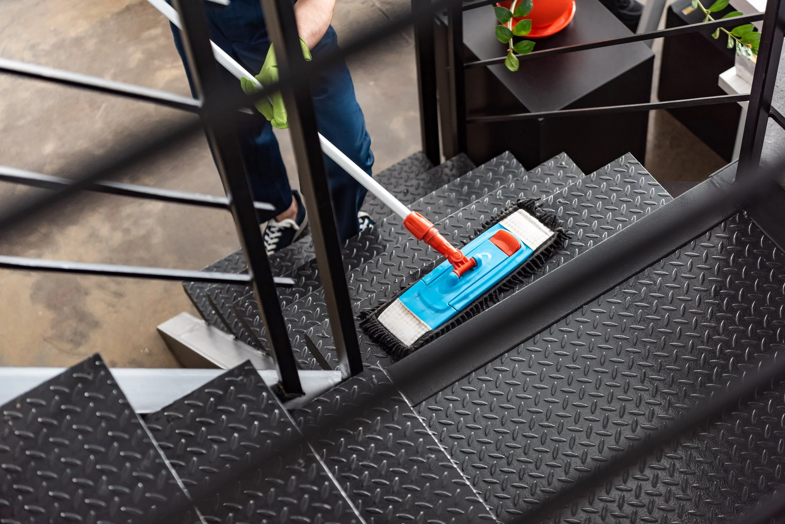 Person mopping black metal staircase with a blue and white mop head, metal stairs, and black railing.