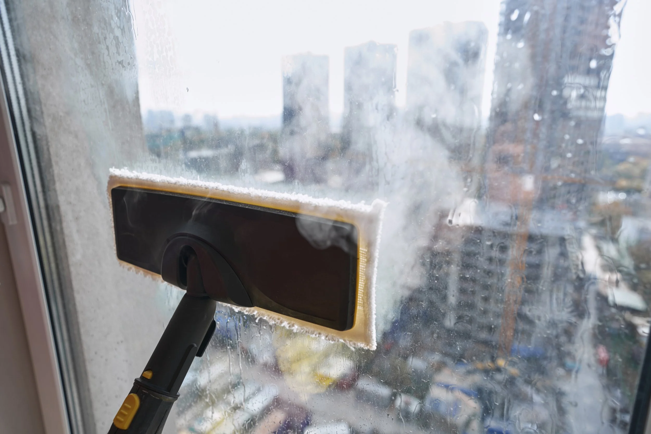 A person cleaning a foggy window with a squeegee, removing condensation and dirt from the glass.