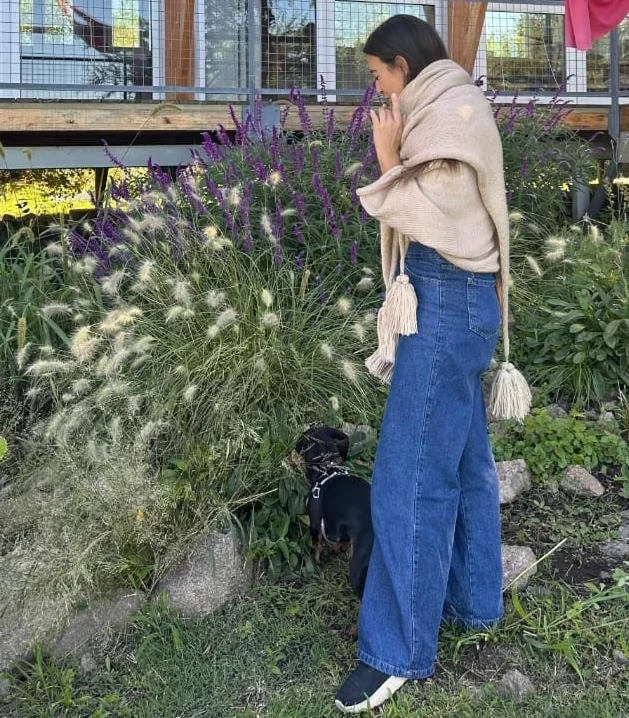 Paisajista, acompañada de un perro pequeño, está en un jardín con salvias y pennisetum en cantero frente a la casa.