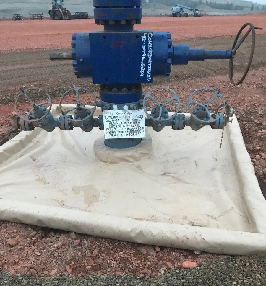A large valve with multiple smaller valves attached, situated on a white covering on red dirt at an outdoor industrial or construction site.
