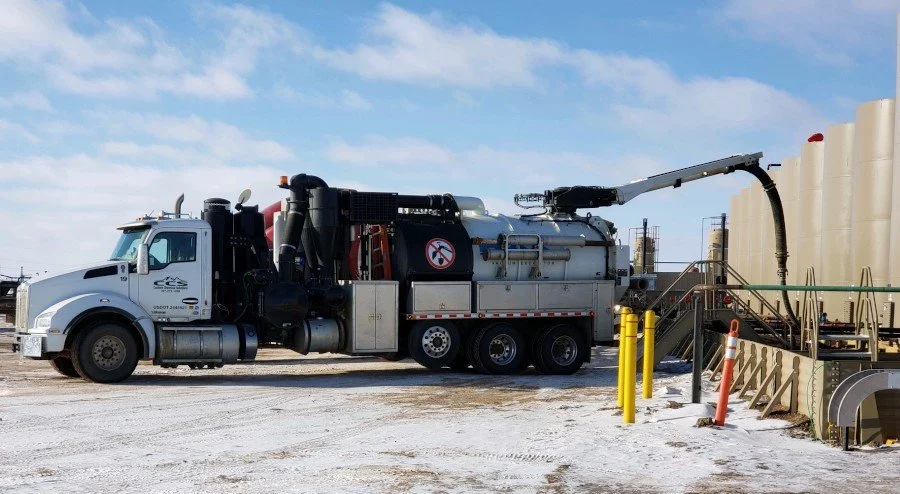 A large industrial vacuum truck parked outdoors in a construction or industrial site with a blue sky and clouds, with a sign indicating no smoking.