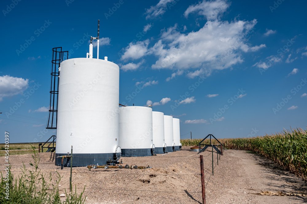 Oil storage tanks in an agricultural field under a blue sky with clouds