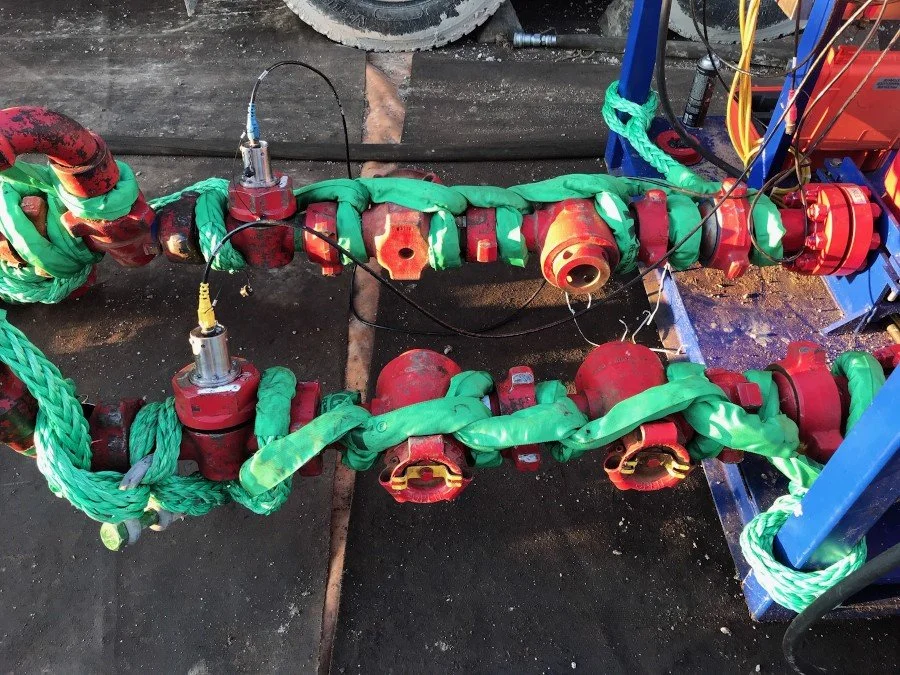 Red industrial valve system with green insulation or padding, connected with wires and hoses, on a dark surface.
