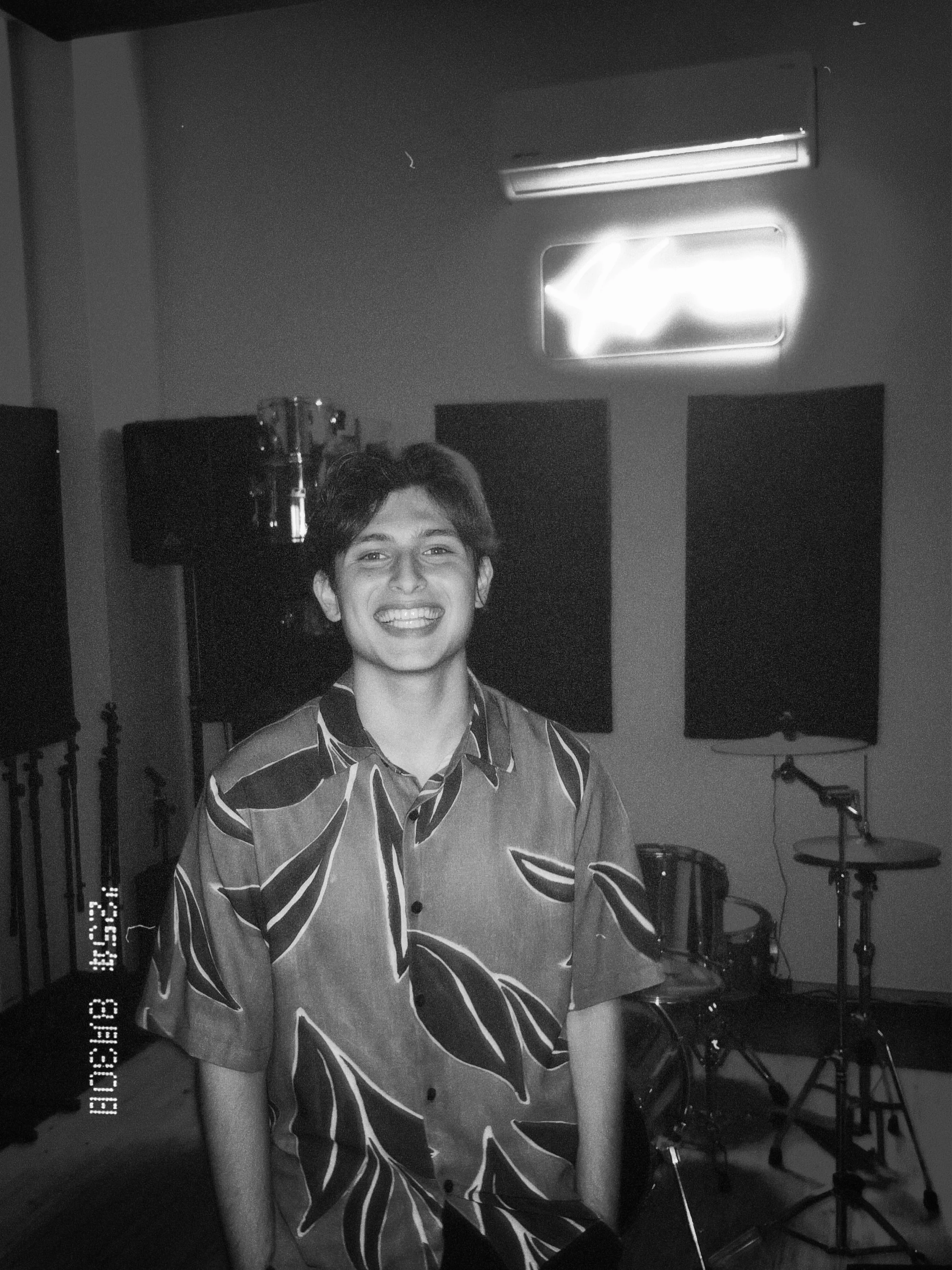 Una persona joven sonriendo en un estudio de grabación, con instrumentos musicales y micrófonos en el fondo.