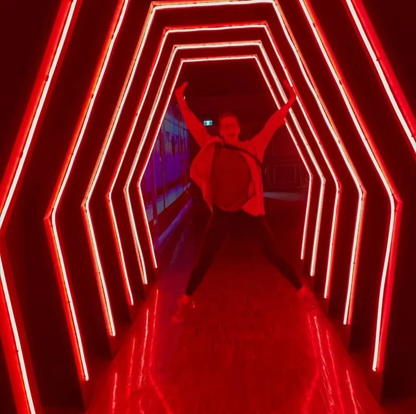 Lisa standing in a tunnel of red neon lights, arms raised in excitement.