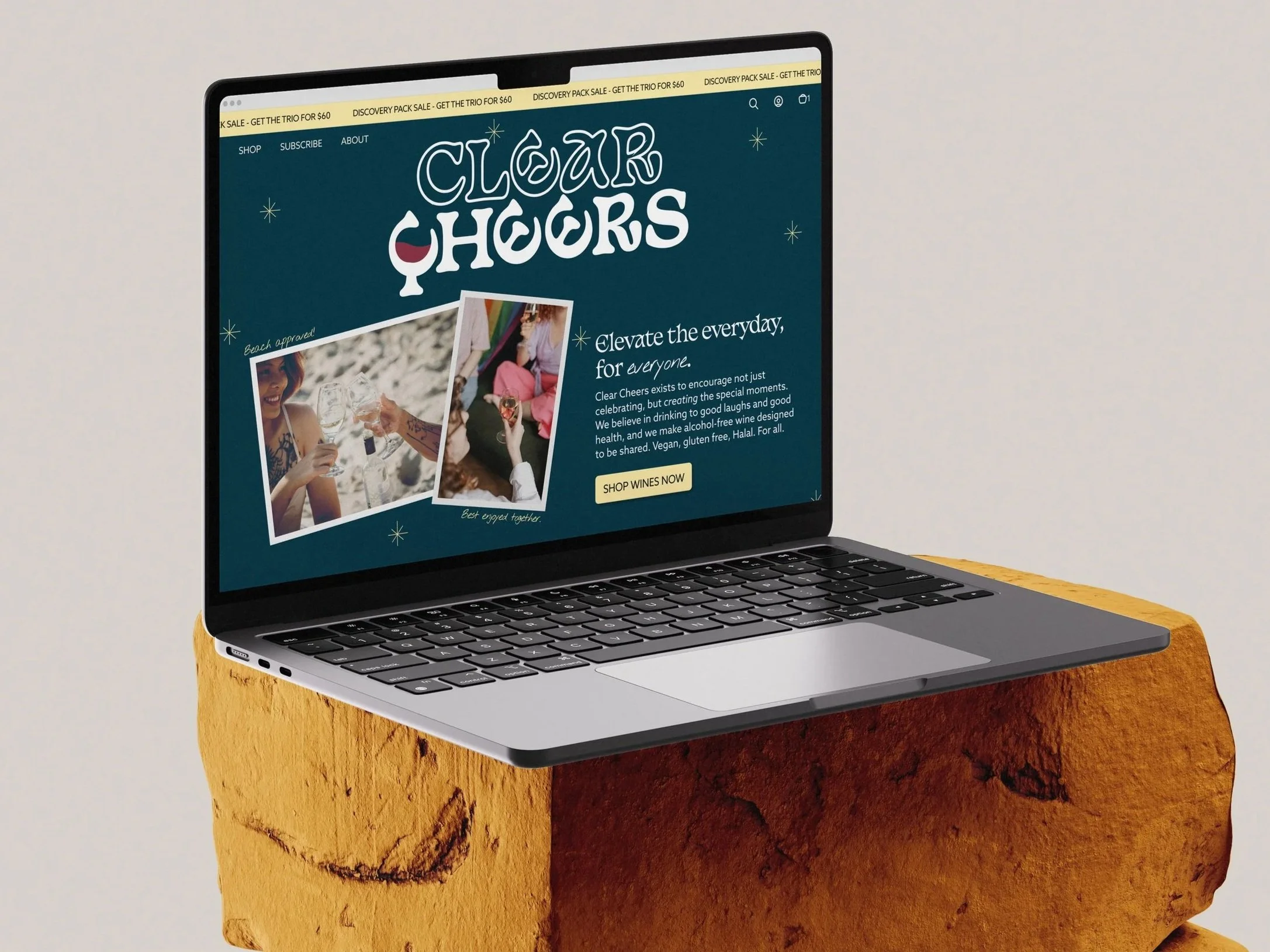 A laptop mockup on a wooden stand displaying the Clear Cheers homepage hero section, with pictures of people enjoying wine.