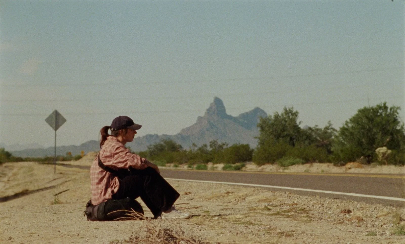 Movie still woman sitting on the side of the road in the dessert on film with a grainy look