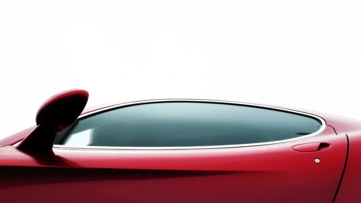 Close-up of a red sports car's driver door and side mirror against a white background.