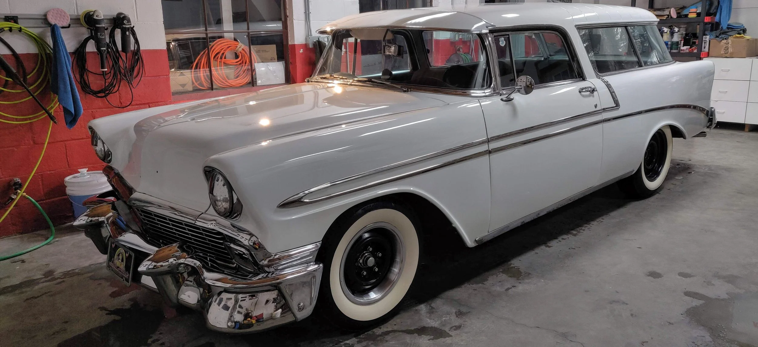 Vintage white car parked in a garage with tools and storage on the walls.