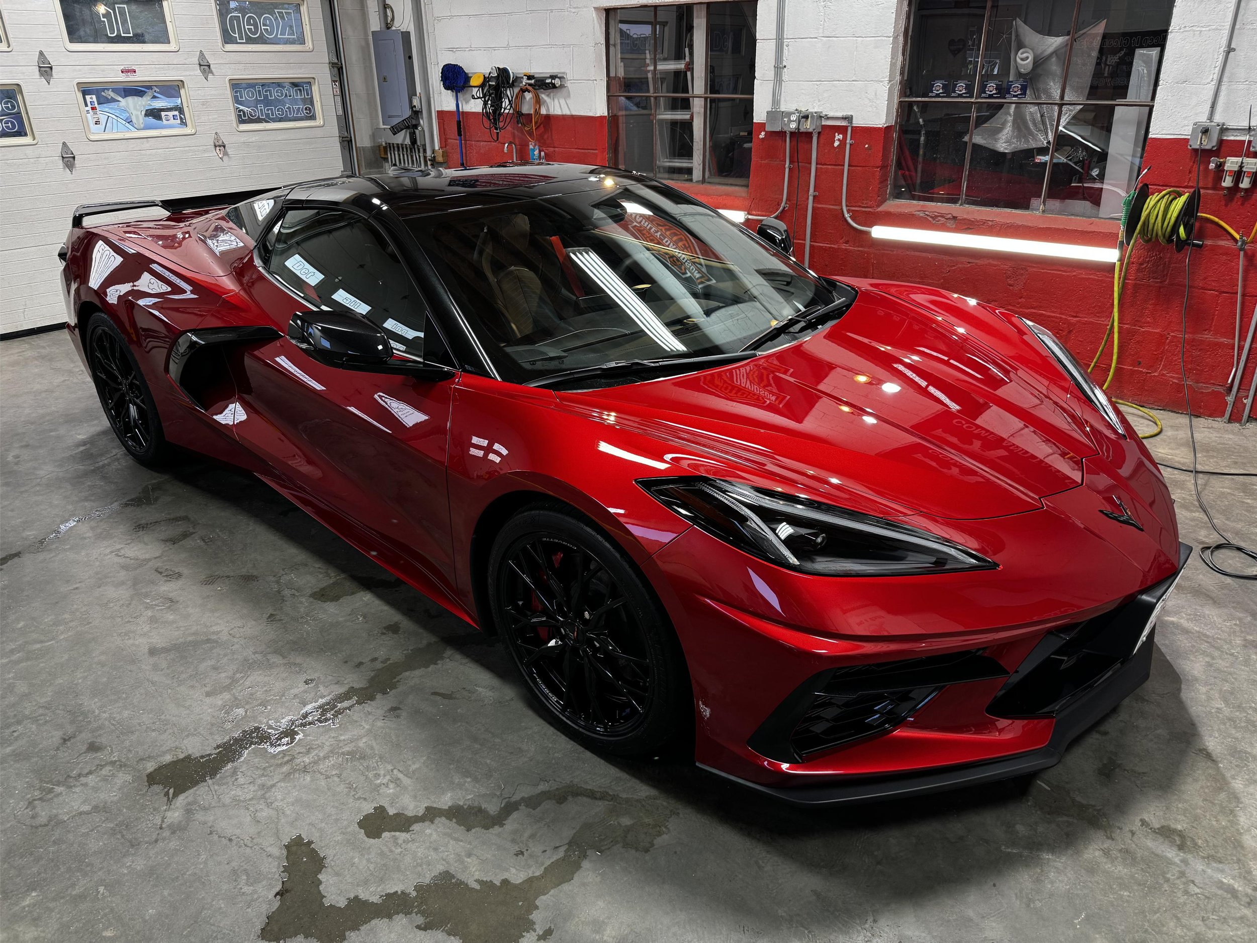 A red sports car parked inside a garage with cleaning and maintenance supplies on the wall and a large garage door in the background.