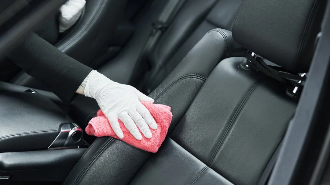 Person wearing a white glove cleaning the back seat of a car with a pink cloth.