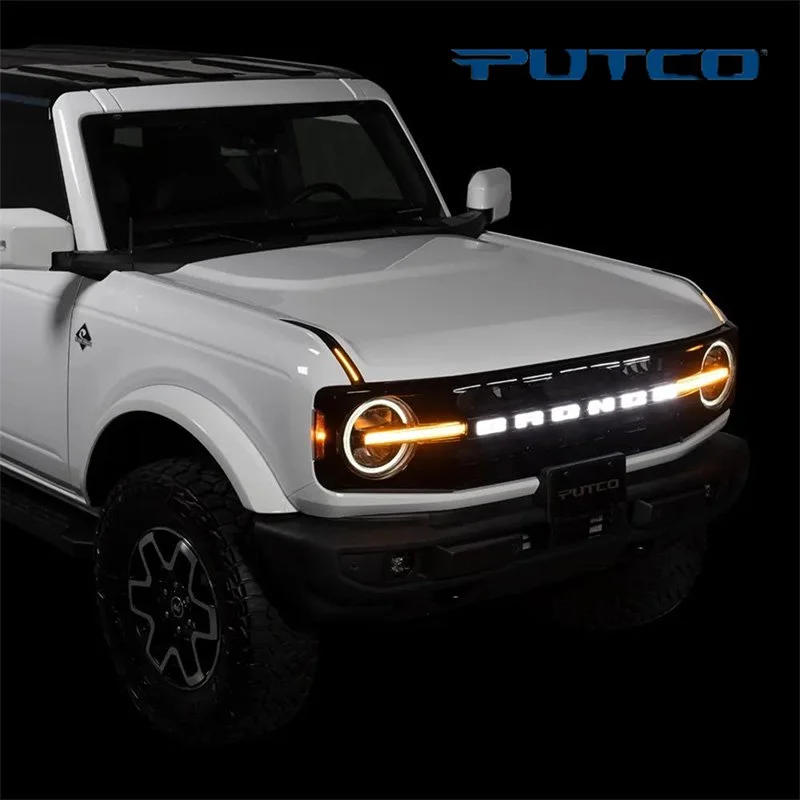 A white electric Ford Bronco vehicle with illuminated front lights and the brand name on the grille, displayed against a black background with the PUTO logo in the top right corner.