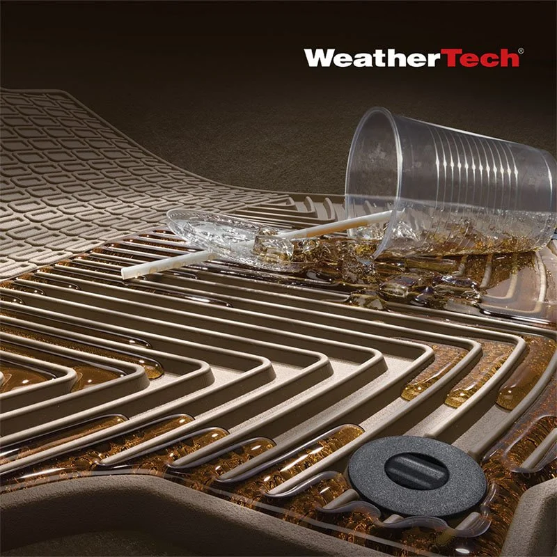Spilled iced coffee on a car's heated floor mats with a clear plastic cup, ice, and a straw, and the WeatherTech logo in the upper right corner.