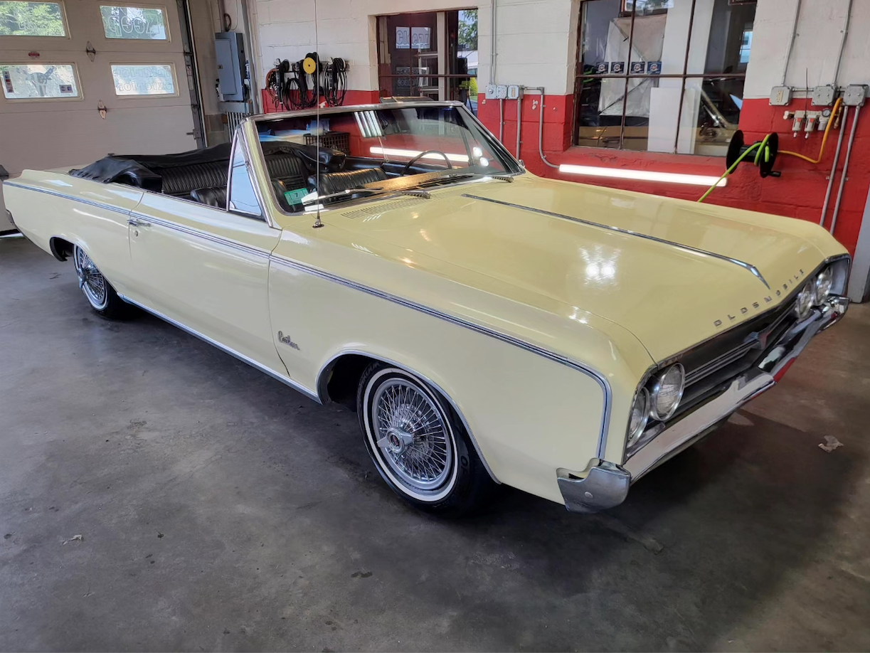 A vintage yellow convertible car parked inside a garage with tools hanging on the wall.