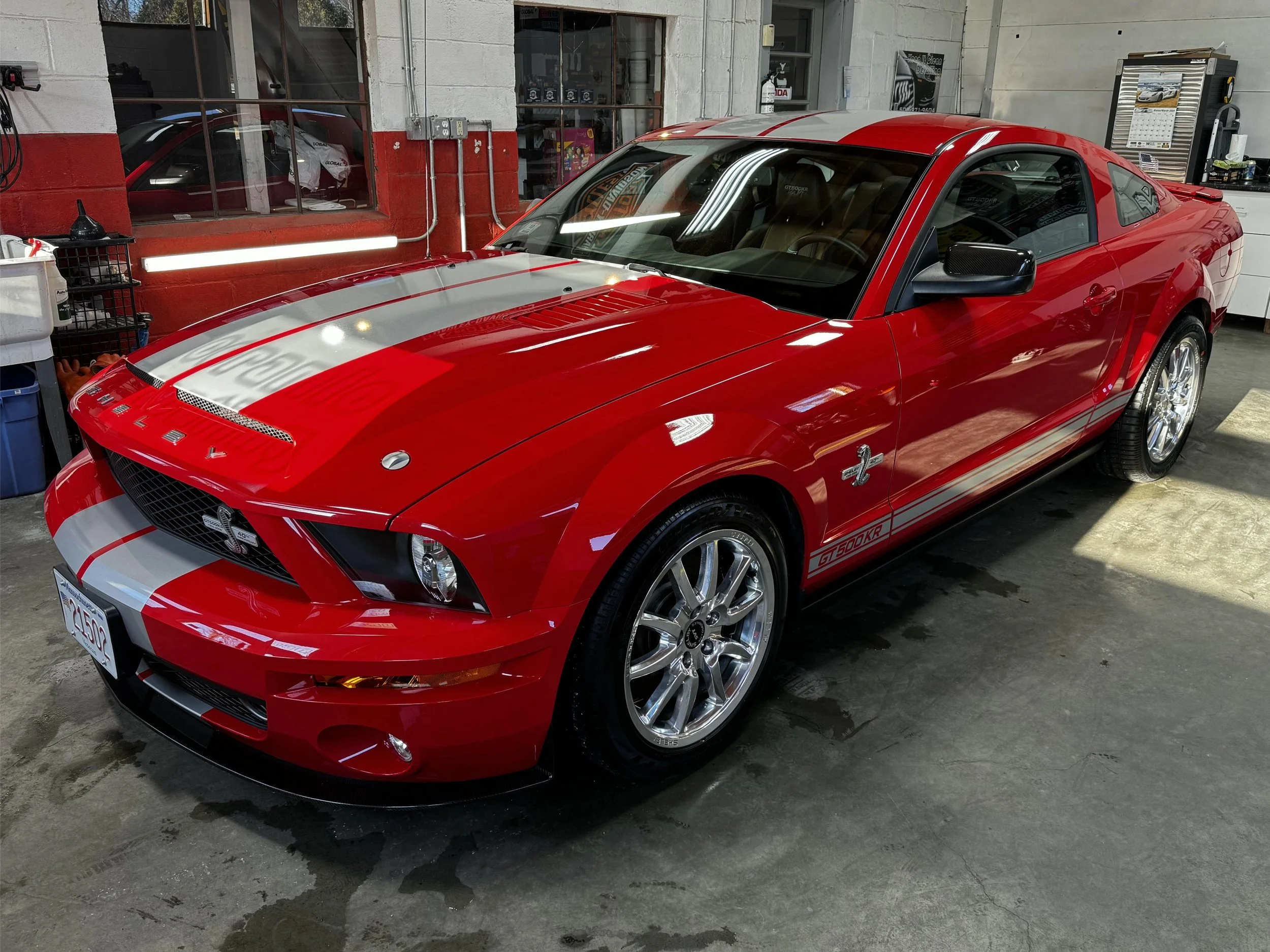 A red and silver Ford Shelby Mustang GT500KR car parked inside a garage or workshop with tools and equipment around.