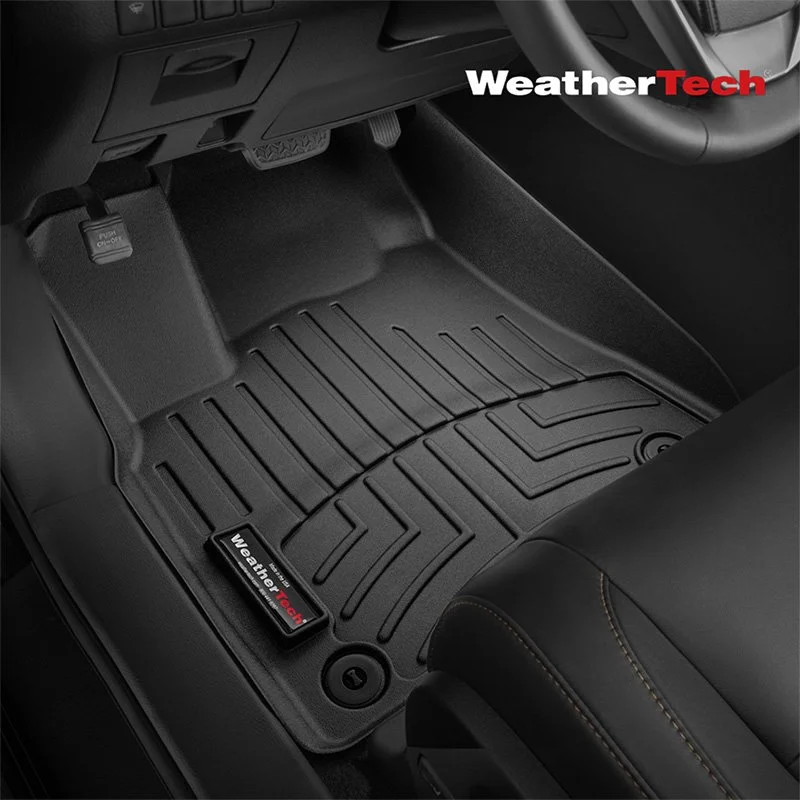 Black rubber WeatherTech vehicle floor mat on car floor with dashboard and gear shift visible.