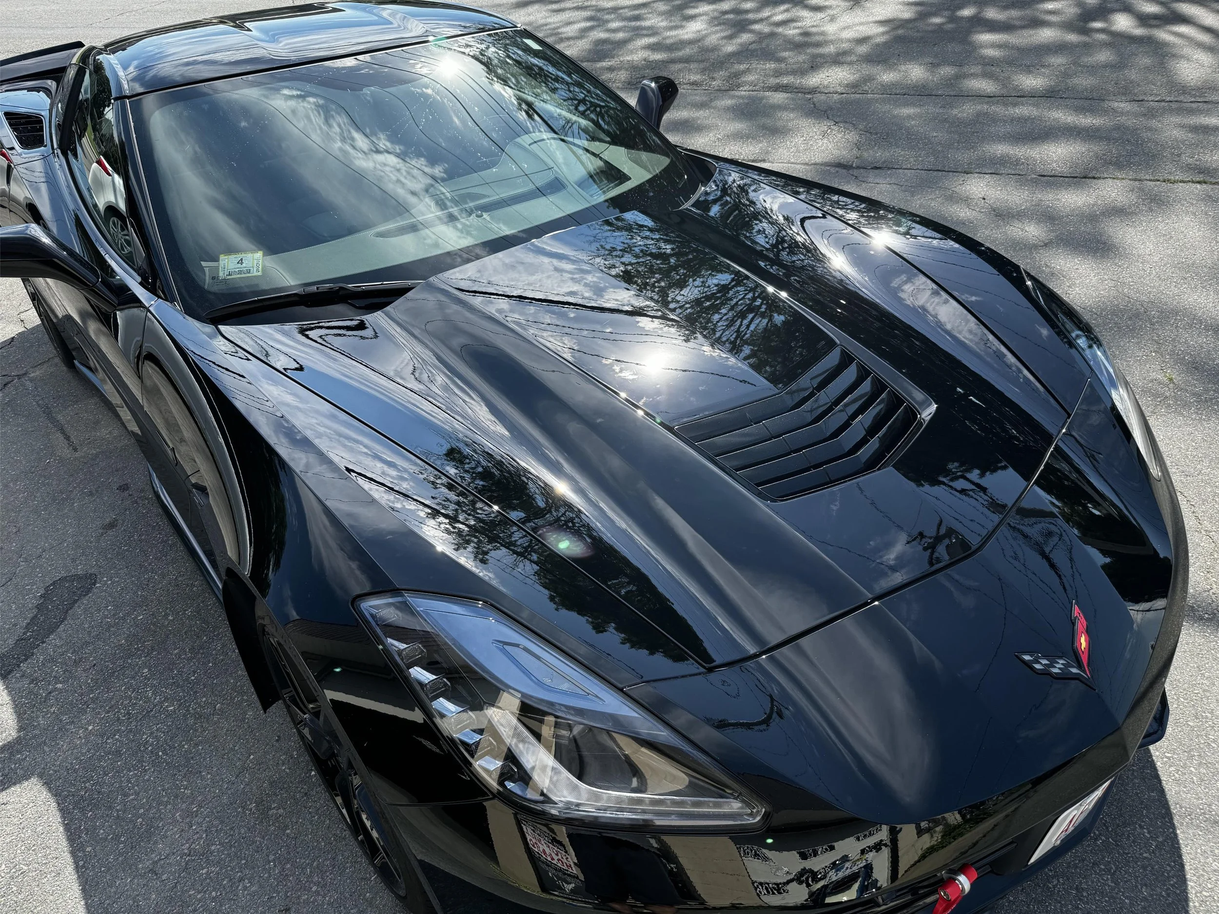 A black sports car parked on a paved surface, with reflections of the sky and trees on its shiny exterior.