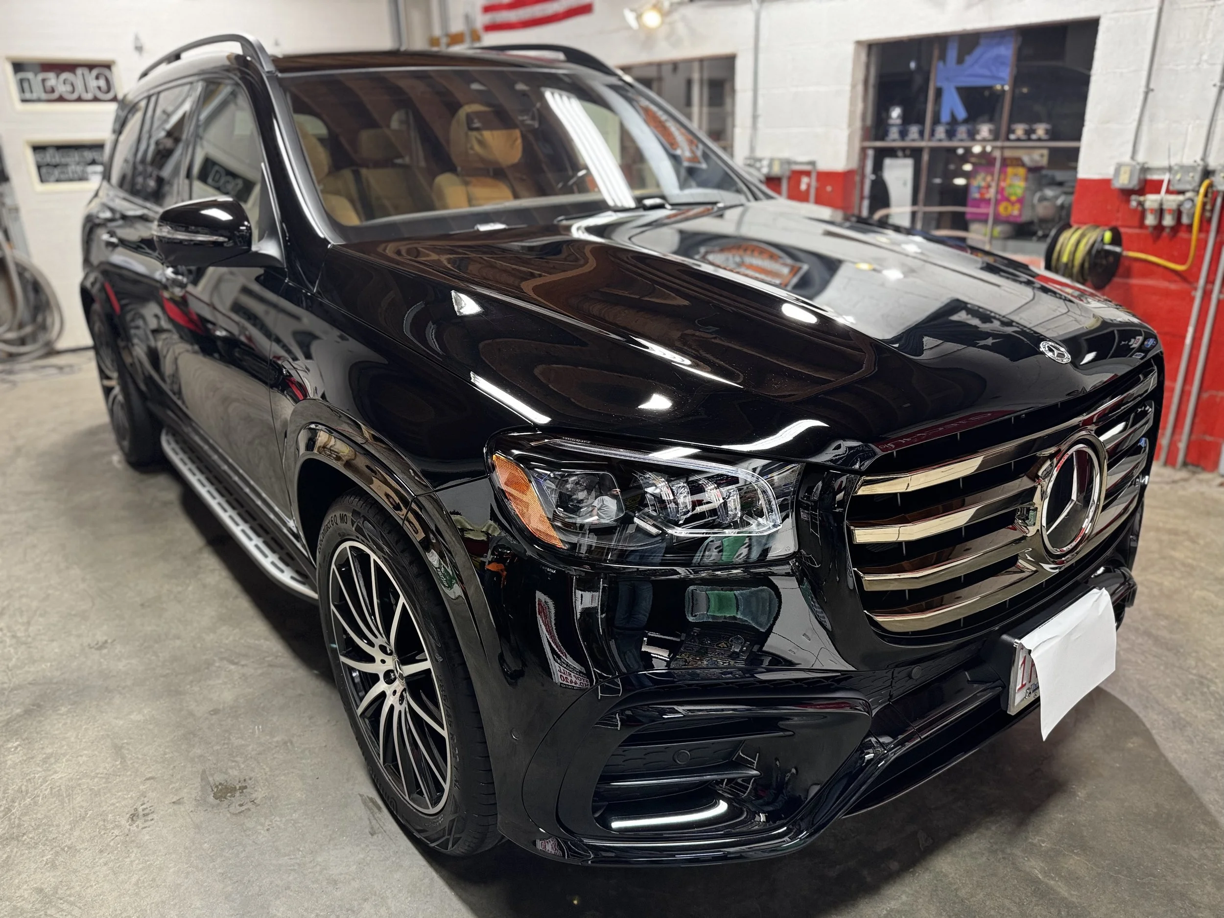 A black Mercedes-Benz SUV parked inside a garage with visible tools and equipment on the wall behind it.
