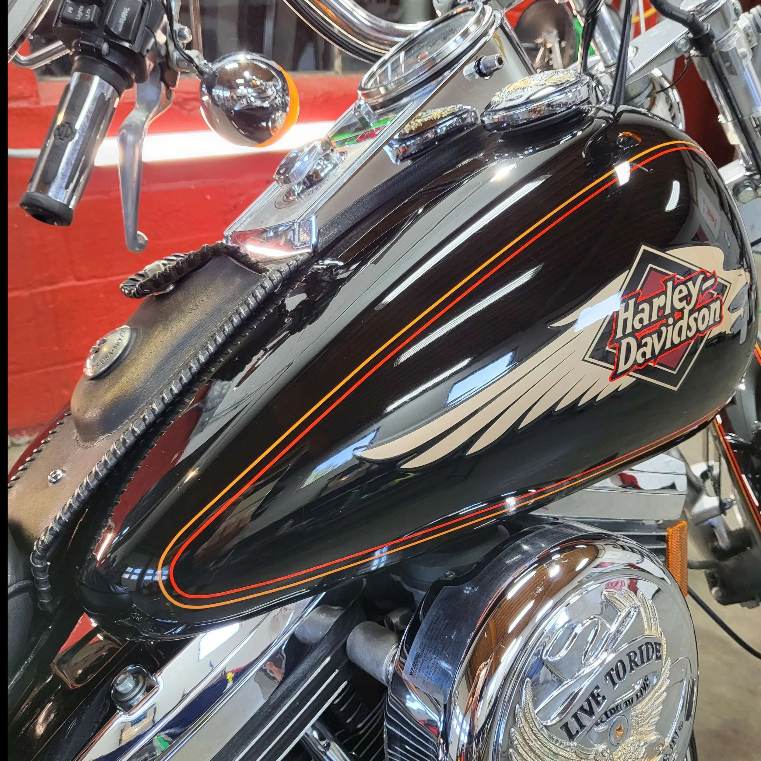 Close-up of a black Harley Davidson motorcycle with chrome details, including the handlebar and fuel tank with a logo.