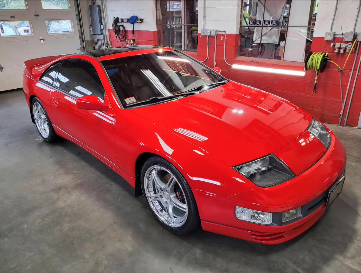 Red sports car parked inside a garage with tools hanging on the wall and a garage door in the background.