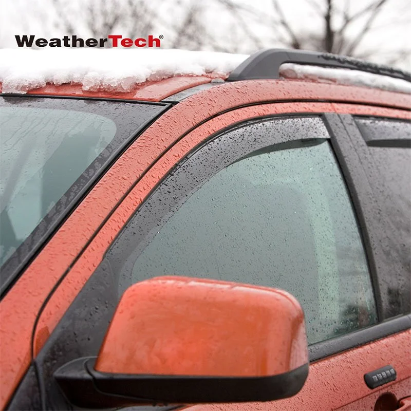 Close-up of a red and black vehicle's front side window, mirror, and roof with snow and rain water droplets visible.