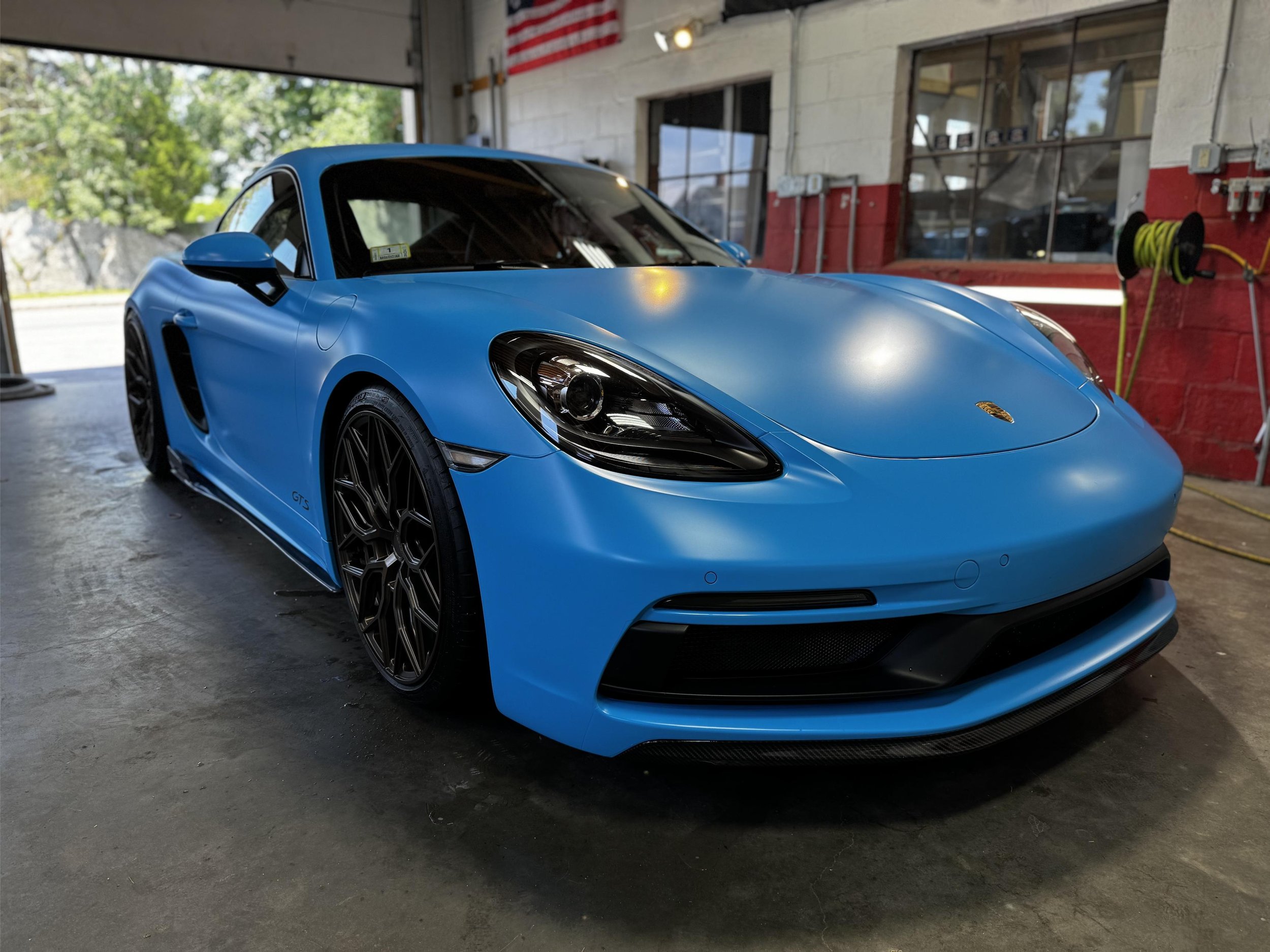 A blue sports car parked inside a garage with red and white walls, large windows, and black wheels with intricate rim designs.