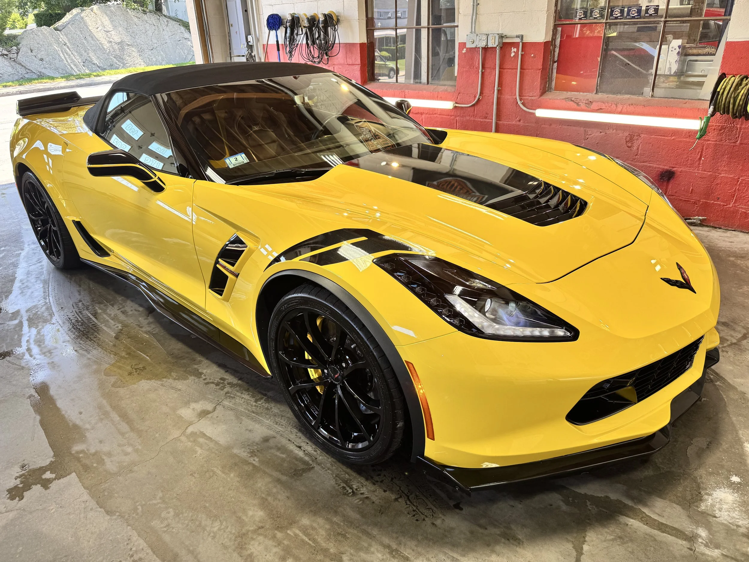 A yellow Chevrolet Corvette with a black convertible top parked inside a garage.