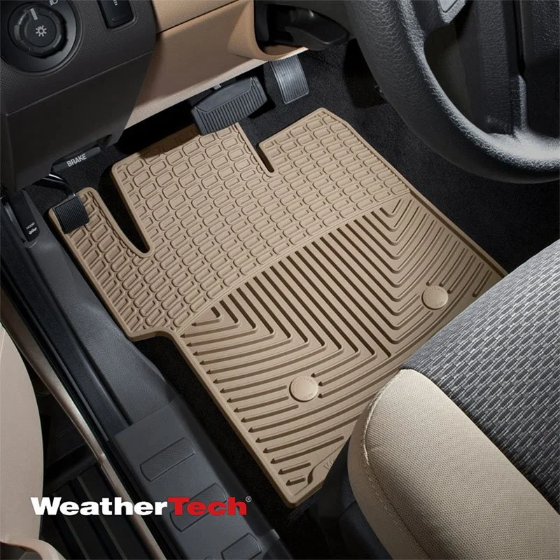 A beige rubber car floor mat with textured patterns inside a vehicle, placed on the driver's side floor near the pedals and seat.