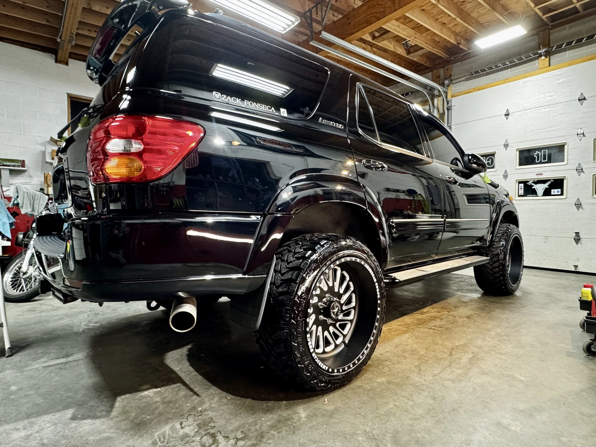 Black SUV parked inside a garage with a garage door, a bicycle to the left, and various garage items stored around.
