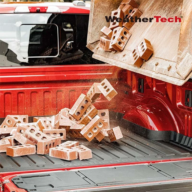 A red pickup truck with a wooden bed liner, dropping bricks onto the truck bed. The logo 'WeatherTech' is visible on the wooden liner.