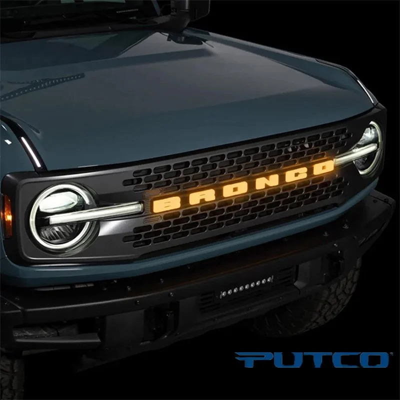Close-up of a car's front grille with a custom illuminated sign reading 'BAD' and the brand name PUTO in the bottom right corner.