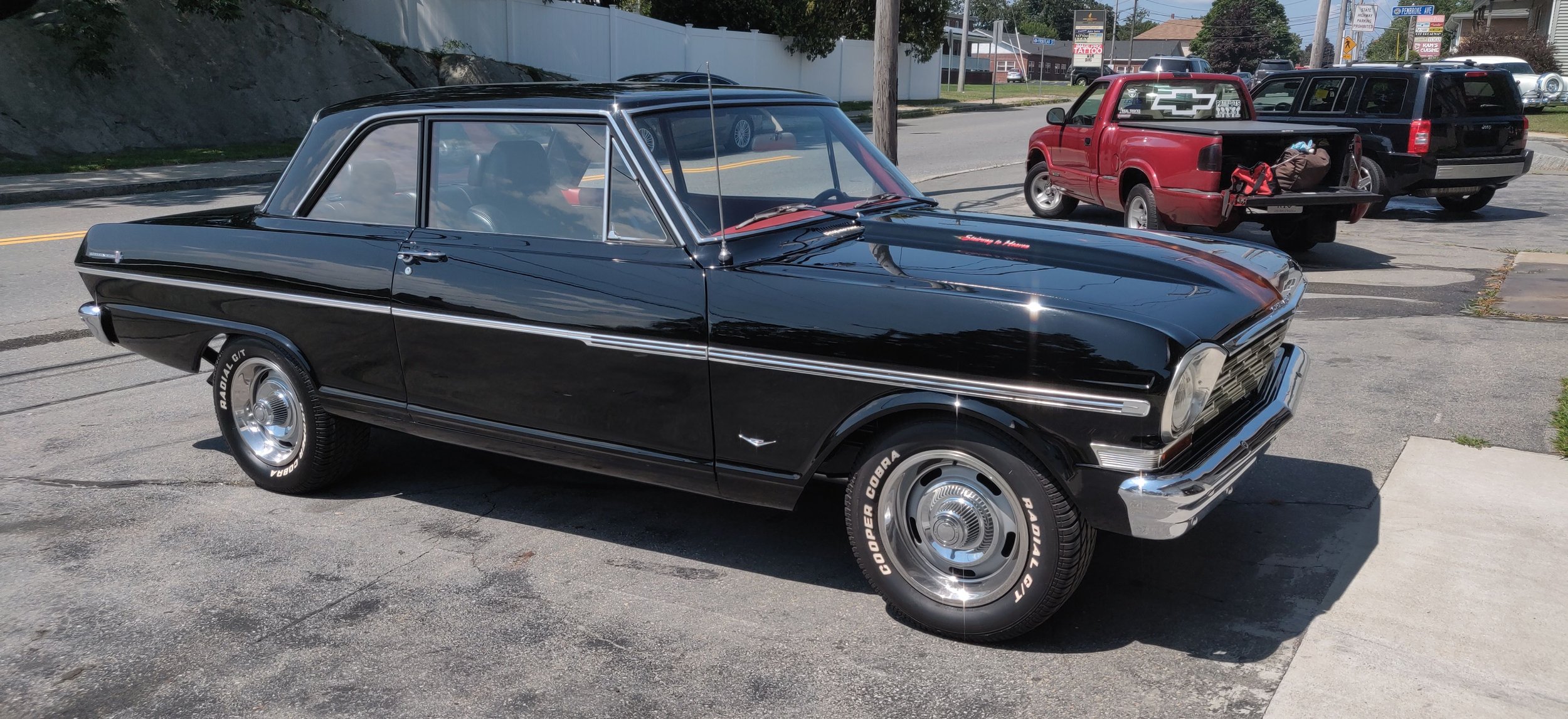 A vintage black car parked on a city street with other vehicles in the background.