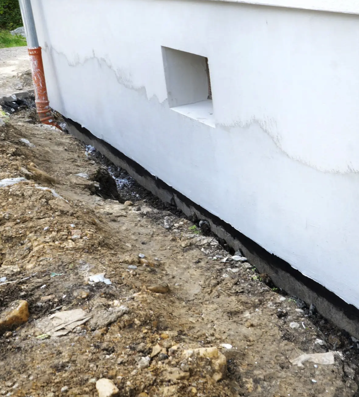 Außenwand eines Gebäudes mit einem kleinen rechteckigen Fenster, umgeben von Erde und Bauarbeiten