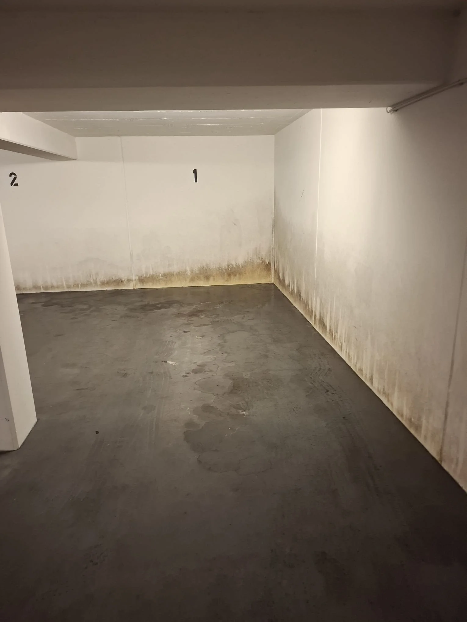 Ein leerer, dunkler Parkbereich oder Keller mit weißen, leicht verschmutzten Wänden, die Nummern 1 und 2 sind auf der Wand zu sehen.
