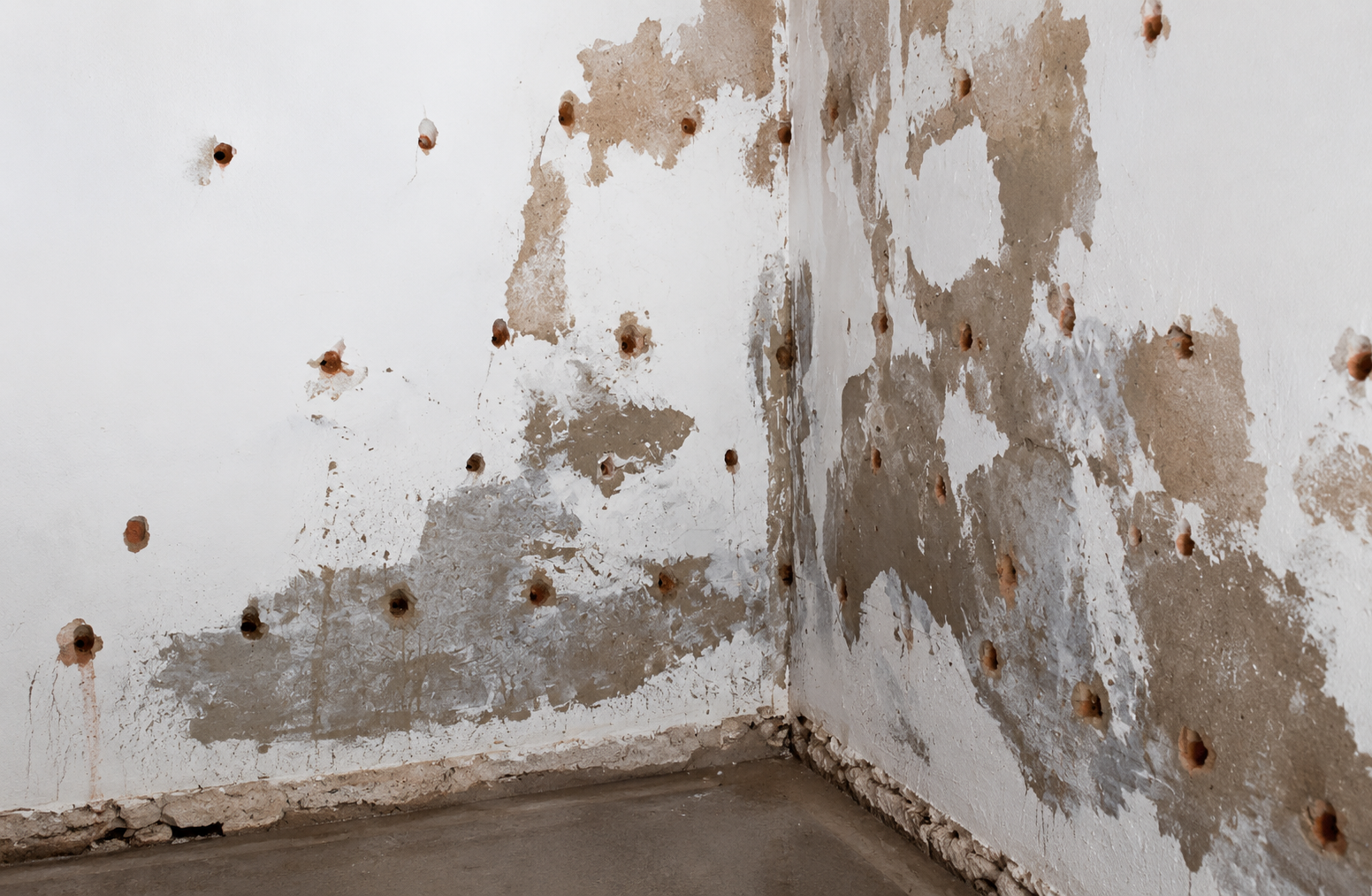 Renovierungsarbeiten an einer Wand mit mehreren Bohrlöchern, Putz und Lackabplatzungen in einem Raum.