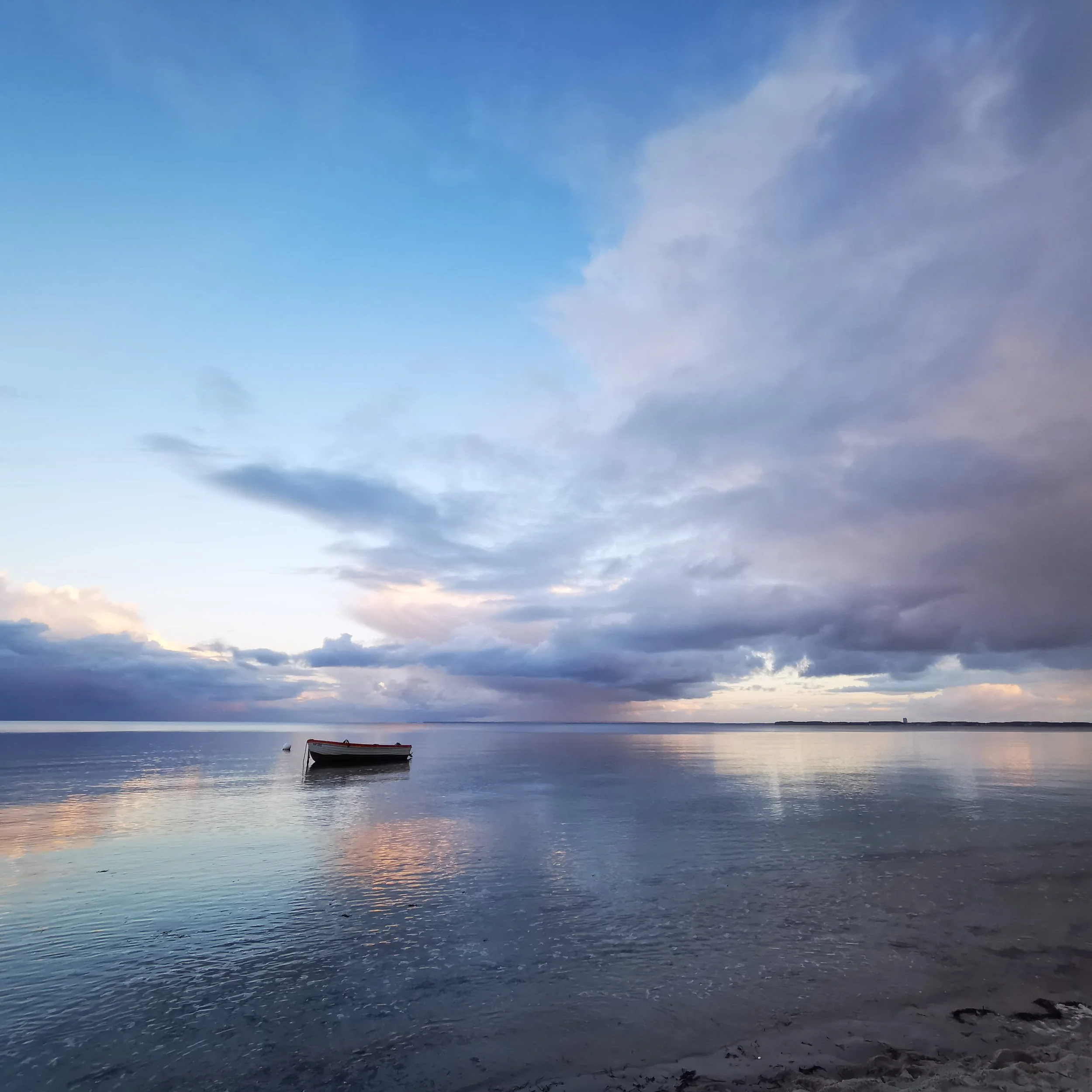 Ein ruhiger See bei Sonnenuntergang mit einem kleinen Boot im Wasser, ein Himmel mit Wolken und verschiedenen Farben, die den Sonnenuntergang spiegeln.