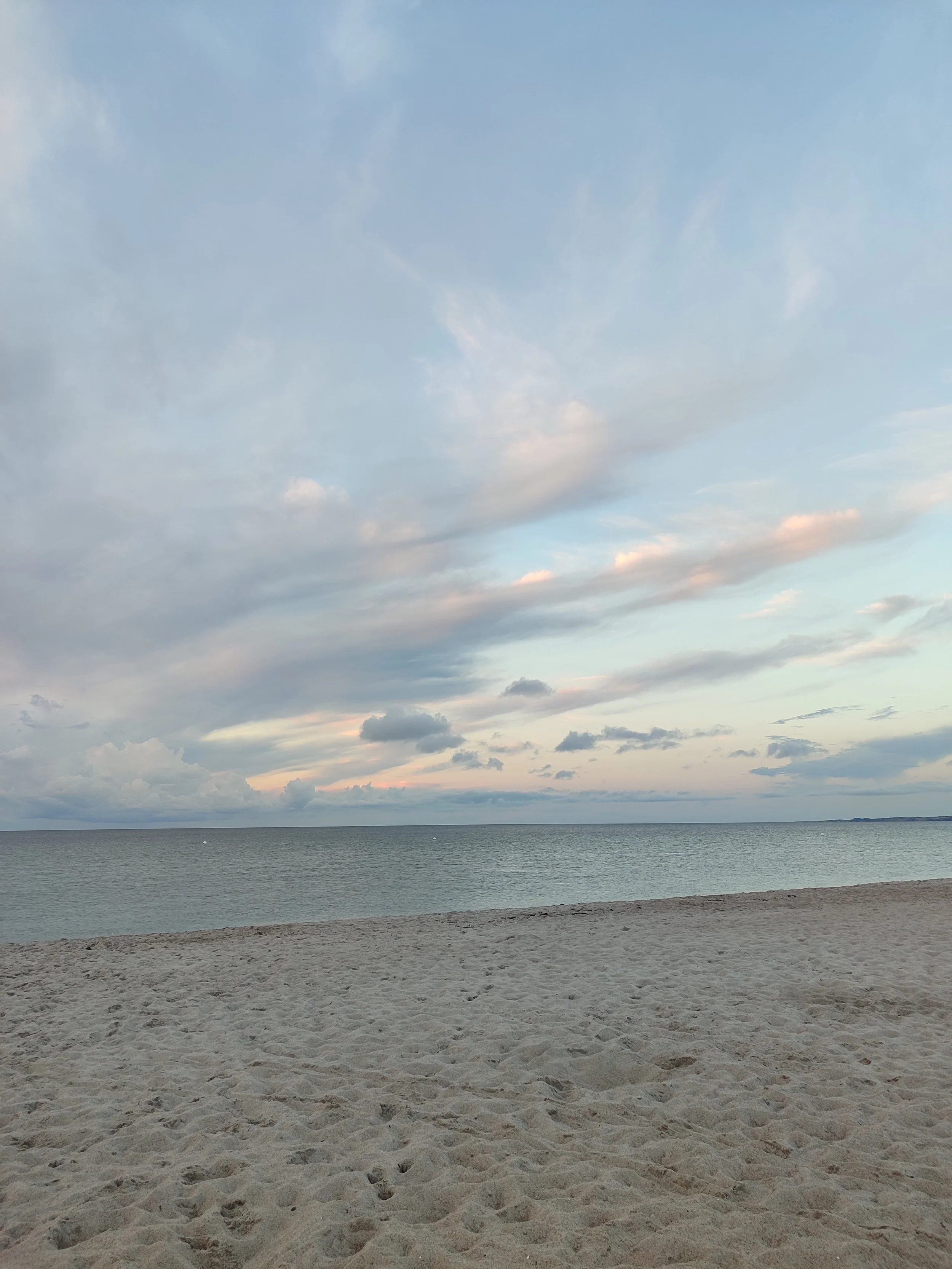 Straand mit Sand am Ufer des Meeres unter einem Himmel mit Wolken.