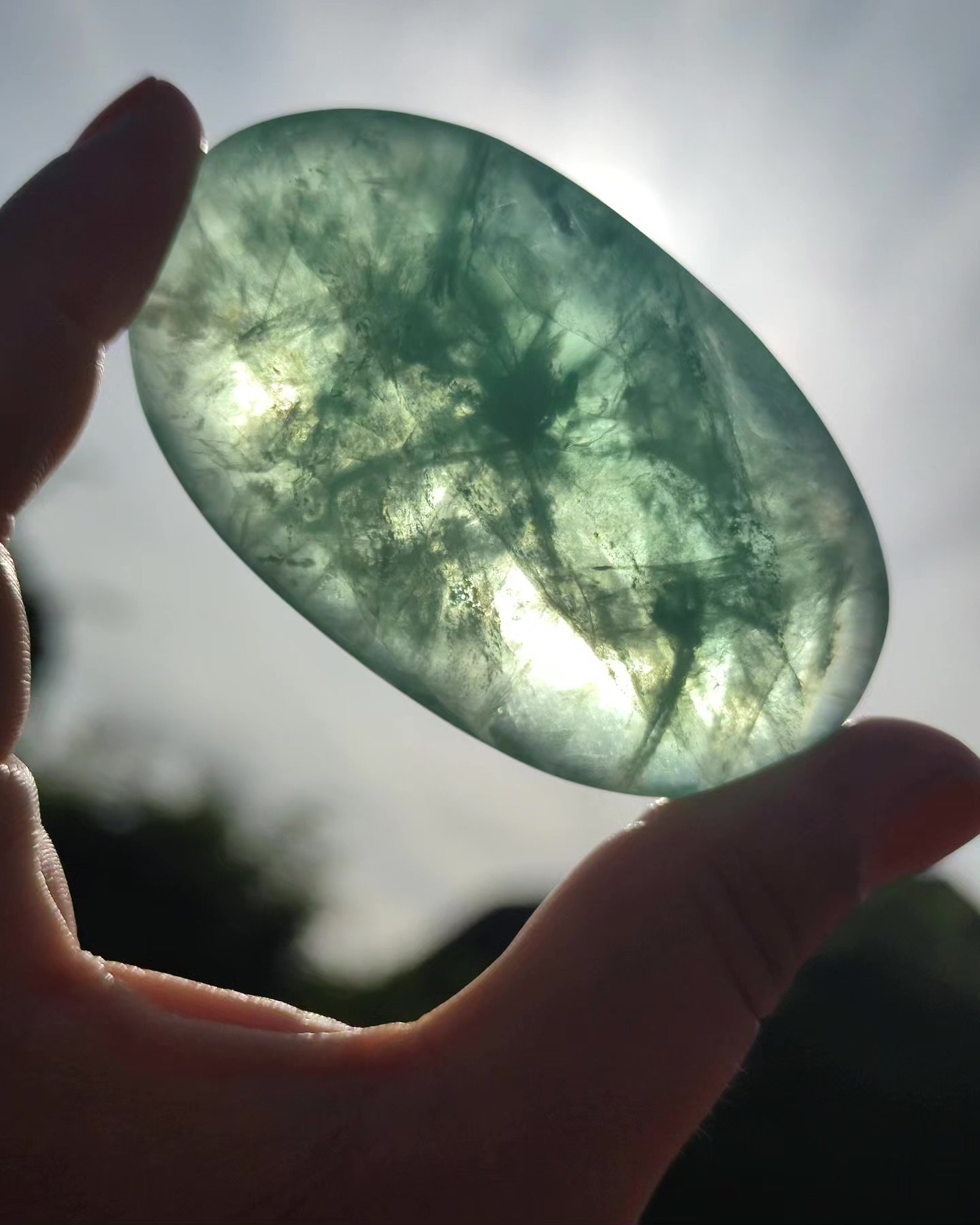 Hand hält eine grüne Jade- oder Edelsteinschale vor hellem Licht, durch das die innere Struktur sichtbar ist.