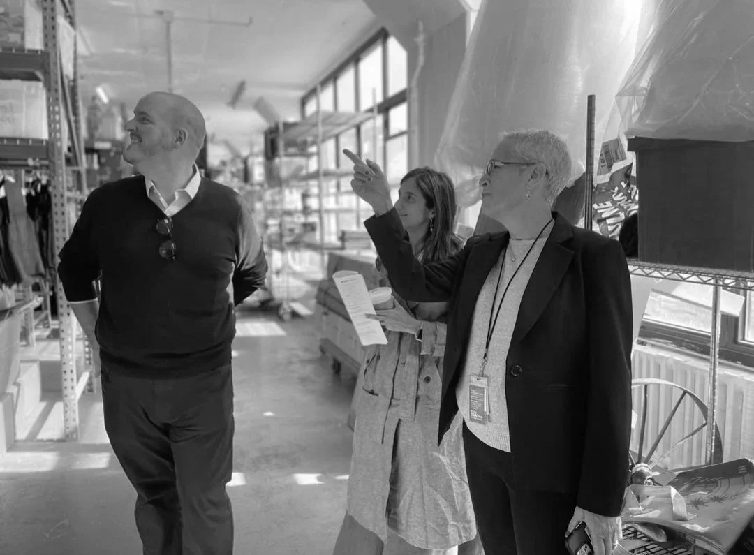 Three adults in an industrial-style store or workspace, with two men and one woman, one man pointing and talking, the others listening.