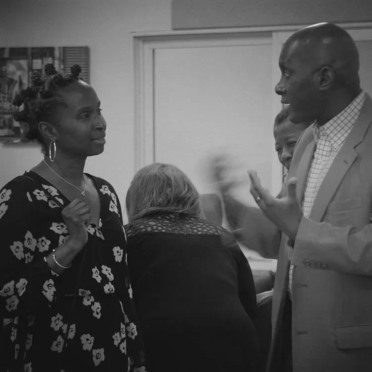 Group of four people engaged in conversation indoors, two women and two men, with bookshelves in background.