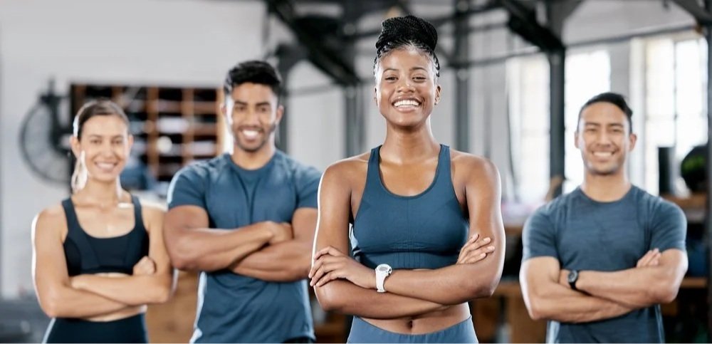 Group of four diverse fit people smiling and standing with arms crossed in a gym.