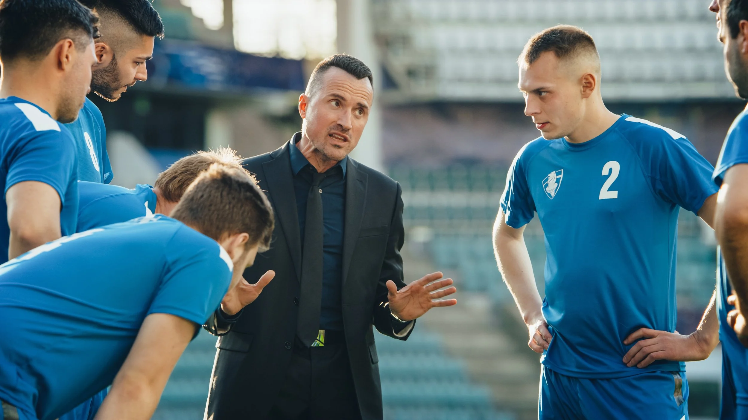 A soccer coach giving instructions to a team of players during a timeout on the field.