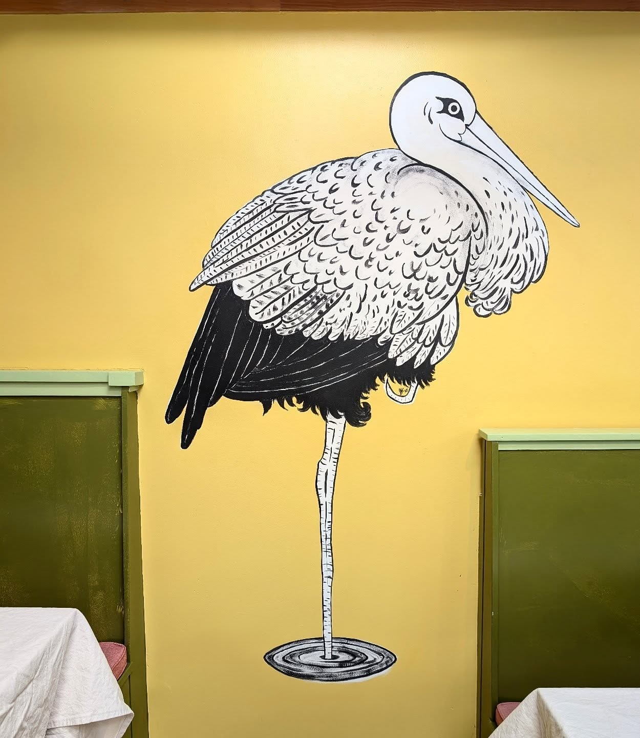 a hand-painted artistic piece which shows a giant stork on a brilliant yellow wall. the stork represents ecological balance and harmony between france and germany. Where French and German cuisine meet.