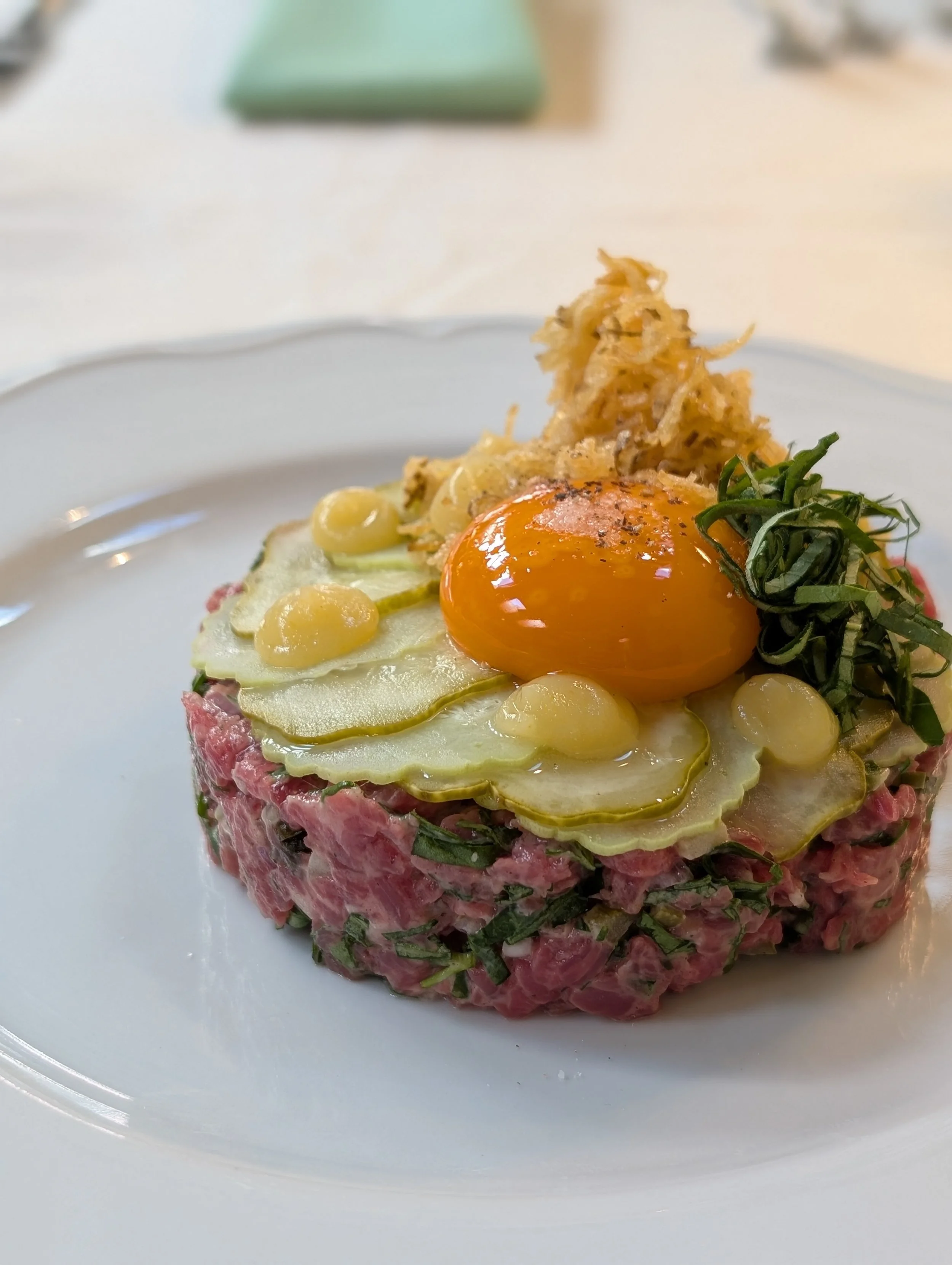 Fresh Teres Major Beef Tartare with egg yolk, aioli, crispy potatoes, and herbs. A great and well-crafted gluten-free and dairy-free dish.