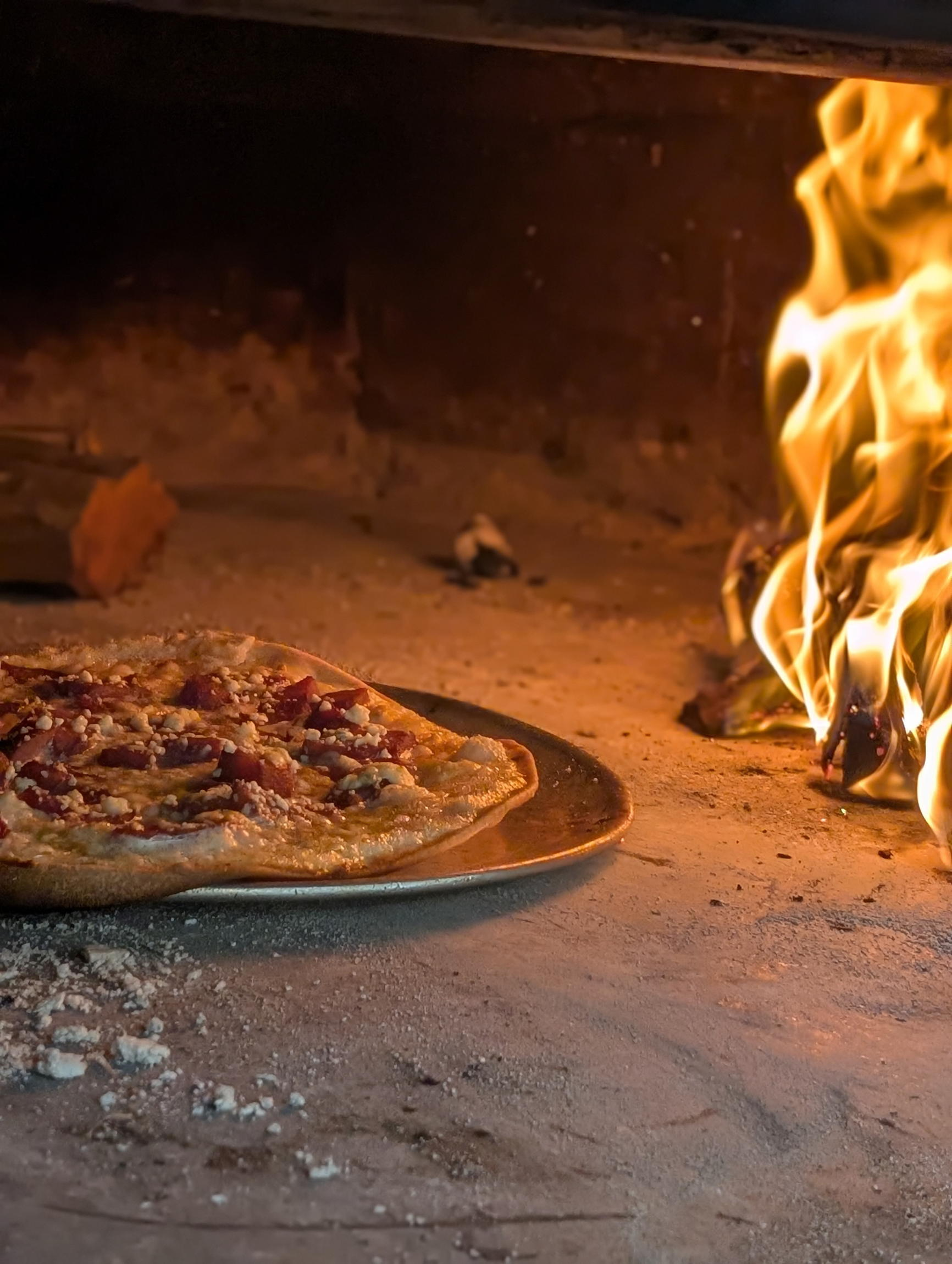 wood fired oven with a warm flame cooking a thin crusted traditional alsatian (french and german) flatbread otherwise known as tarte flambee or flammekueche